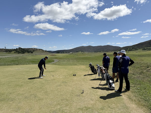 Charles playing a tee shot while his golf group watches.